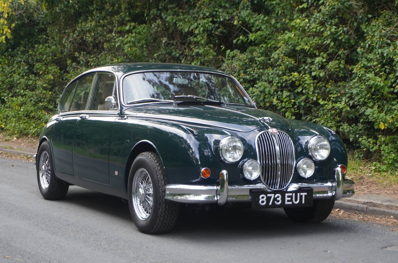 The restomod Jaguar Mk2 873 EUT in British Racing Green on a country road, showing its wire wheels and chrome grille